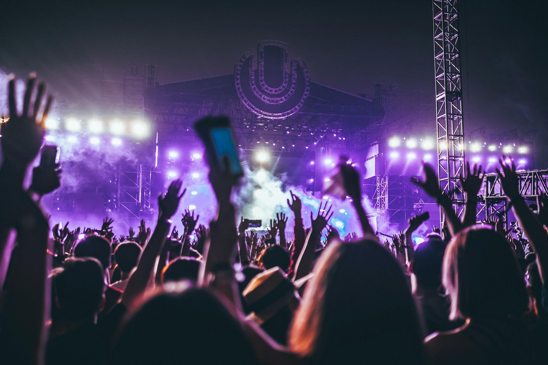 Silhouetted concertgoers raising their hands toward a brightly lit stage